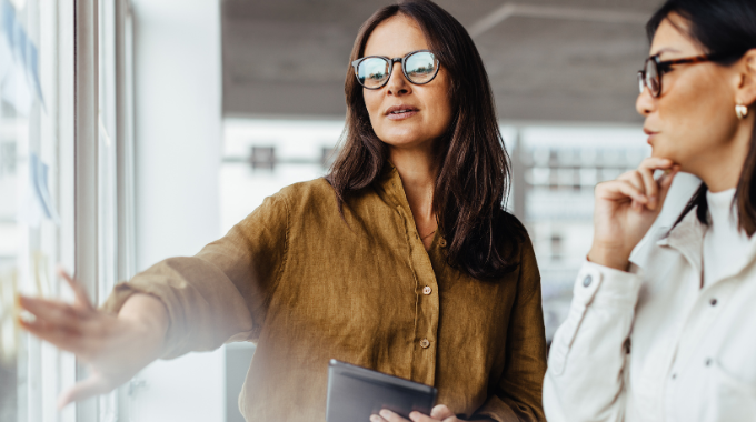 Two women standing new a presentation screen having a discussion.